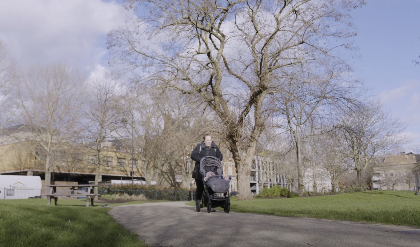 Kvinde der går tur i en park med en baby i klapvogn