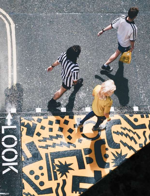 Tre mennesker som går på en vej som er pyntet med maling, set ovenfra